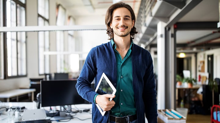 A smiling SME stands confidently at a table in an office space, facing the camera.