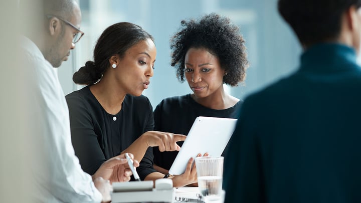 Two women entrepreneurs collaborate at a table, focused on their tablet as they share ideas.