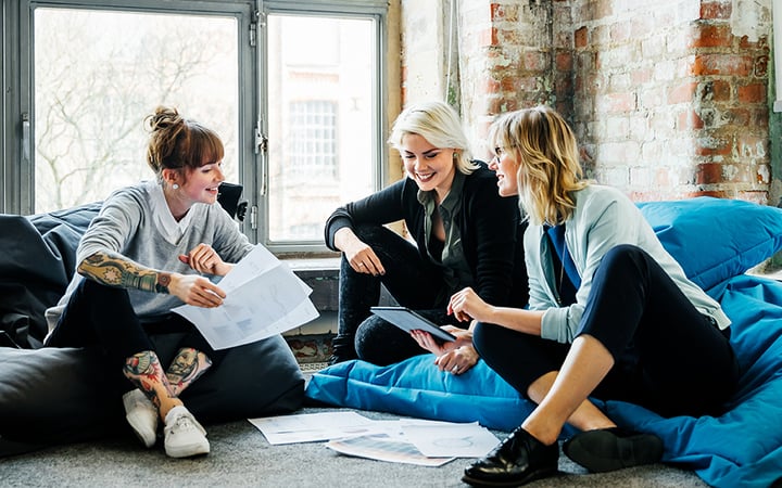 Three women sitting on bean bags with papers on the floor.