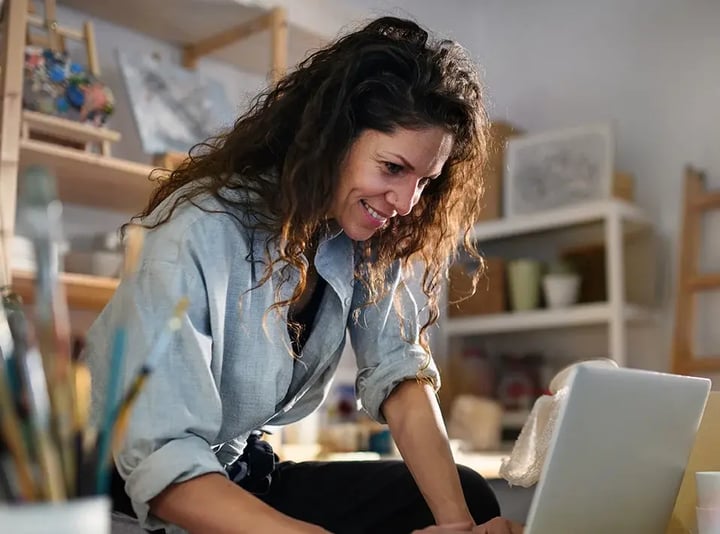 Une femme sourit tout en travaillant sur son ordinateur portable, illustrant un moment de joie et de productivité.