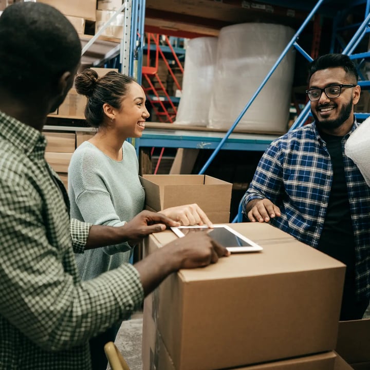 Trois personnes organisant des cartons dans un entrepôt spacieux.