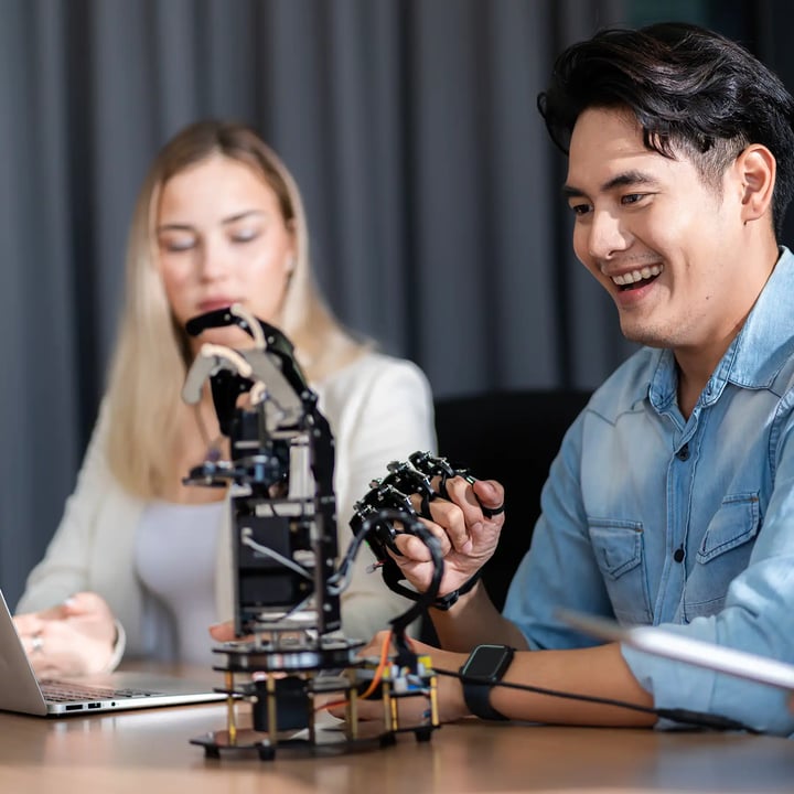 Une femme et un homme assis ensemble testant un bras robotique.