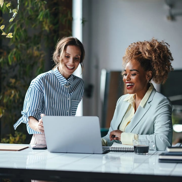 Deux femmes d'affaires souriant et riant en regardant ensemble l'écran d'ordinateur.