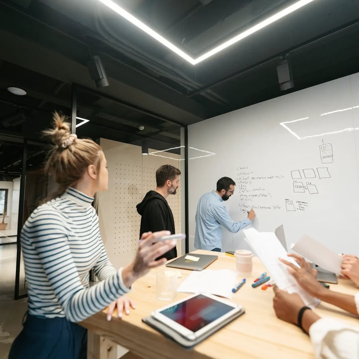 Deux hommes entrepreneurs font un brainstorming dans un bureau, l'un esquissant des idées sur un tableau blanc tandis que l'autre observe attentivement.