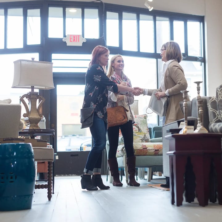 Trois femmes se tiennent ensemble dans une pièce meublée, discutant au milieu du décor et des meubles qui les entourent.