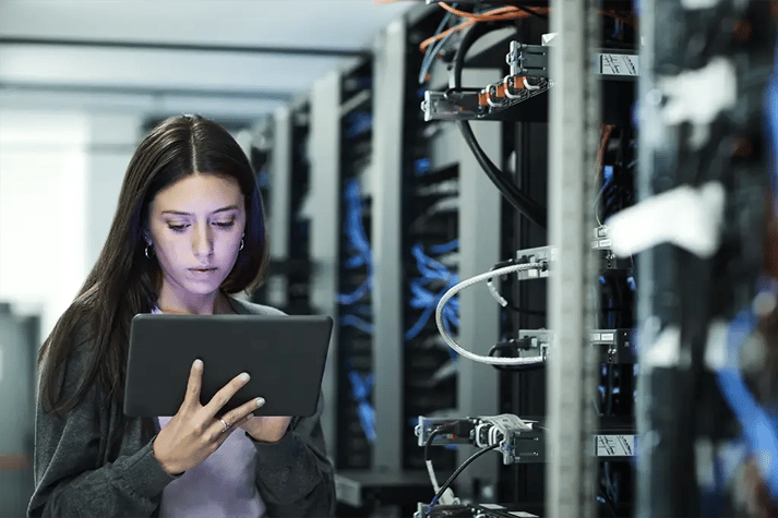 Une femme utilise une tablette informatique entourée de racks de serveurs dans une salle de serveurs de haute technologie.