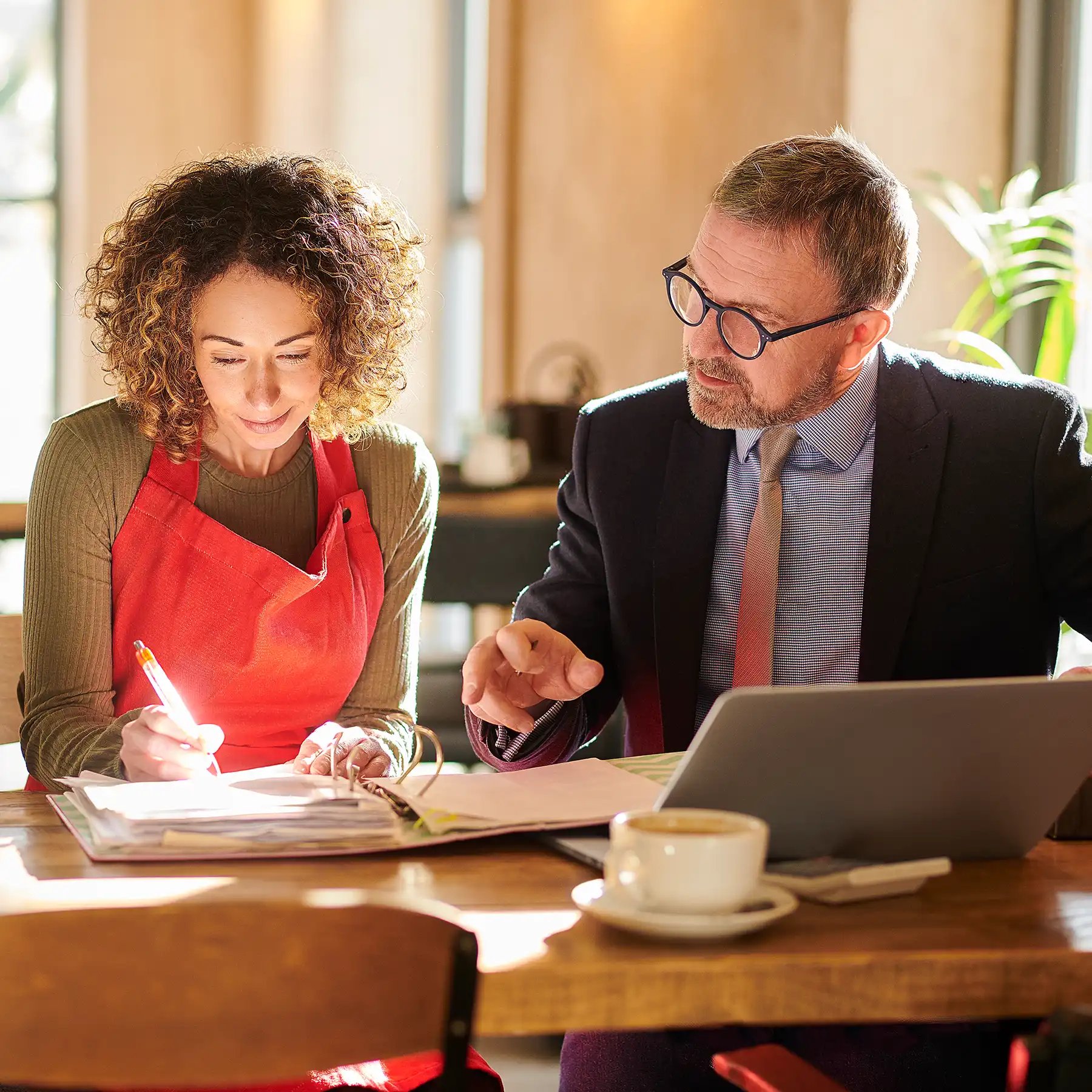 A man and woman in aprons are attentively examining a laptop together, engaged in a collaborative task.