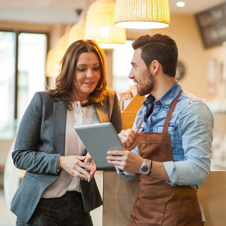 A business owner and his assistant collaborate on a tablet, discussing strategies in a professional setting.