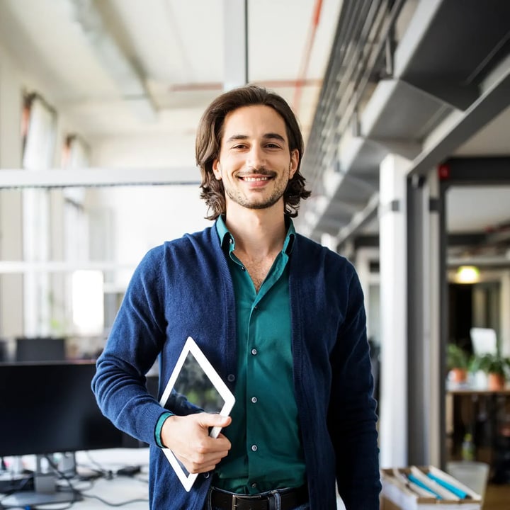 A smiling SME stands confidently at a table in an office space, facing the camera.