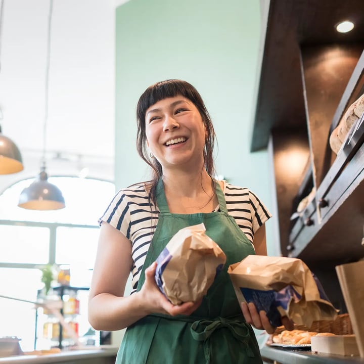 A cheerful woman holding a bag of food, radiating happiness and positivity in her expression.