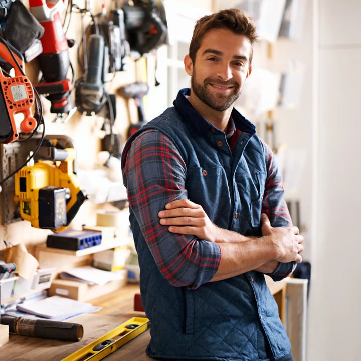 A man poses in front of a wall filled with various tools, showcasing a well-organized workspace.