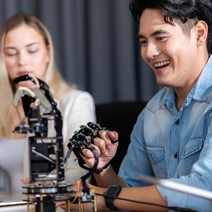 A women and a man sitting together testing a robotic arm