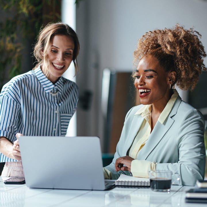 Two business women smiling and laughing looking at computer screen together