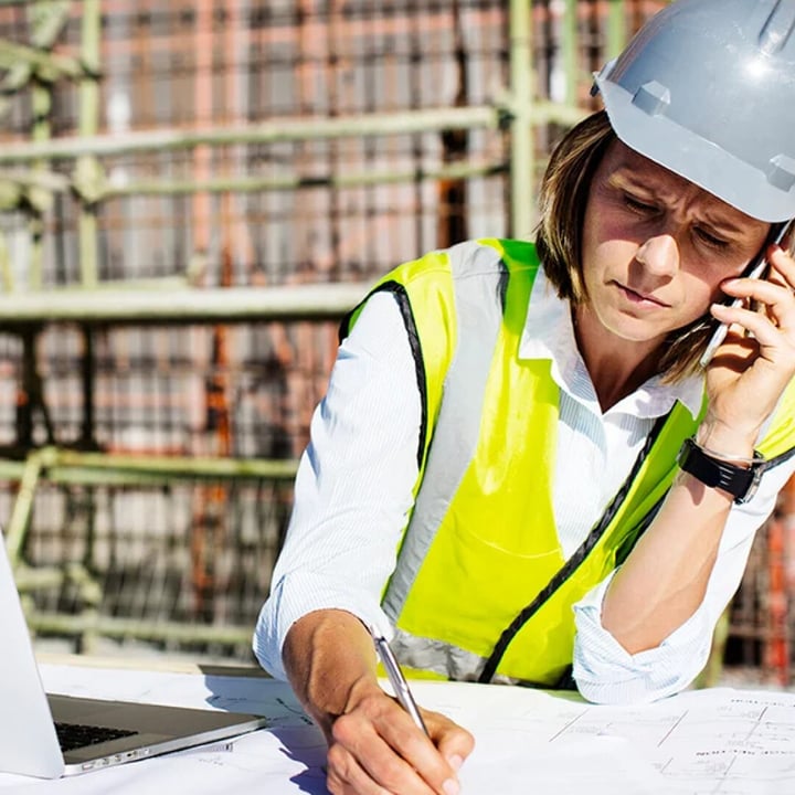 Ouvrière de la construction portant un casque de sécurité, téléphonant et prenant des notes.