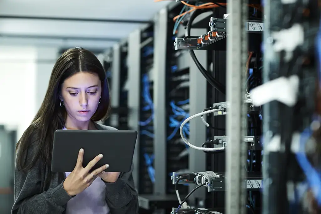 A woman operates a tablet computer while surrounded by server racks in a high-tech server room. 