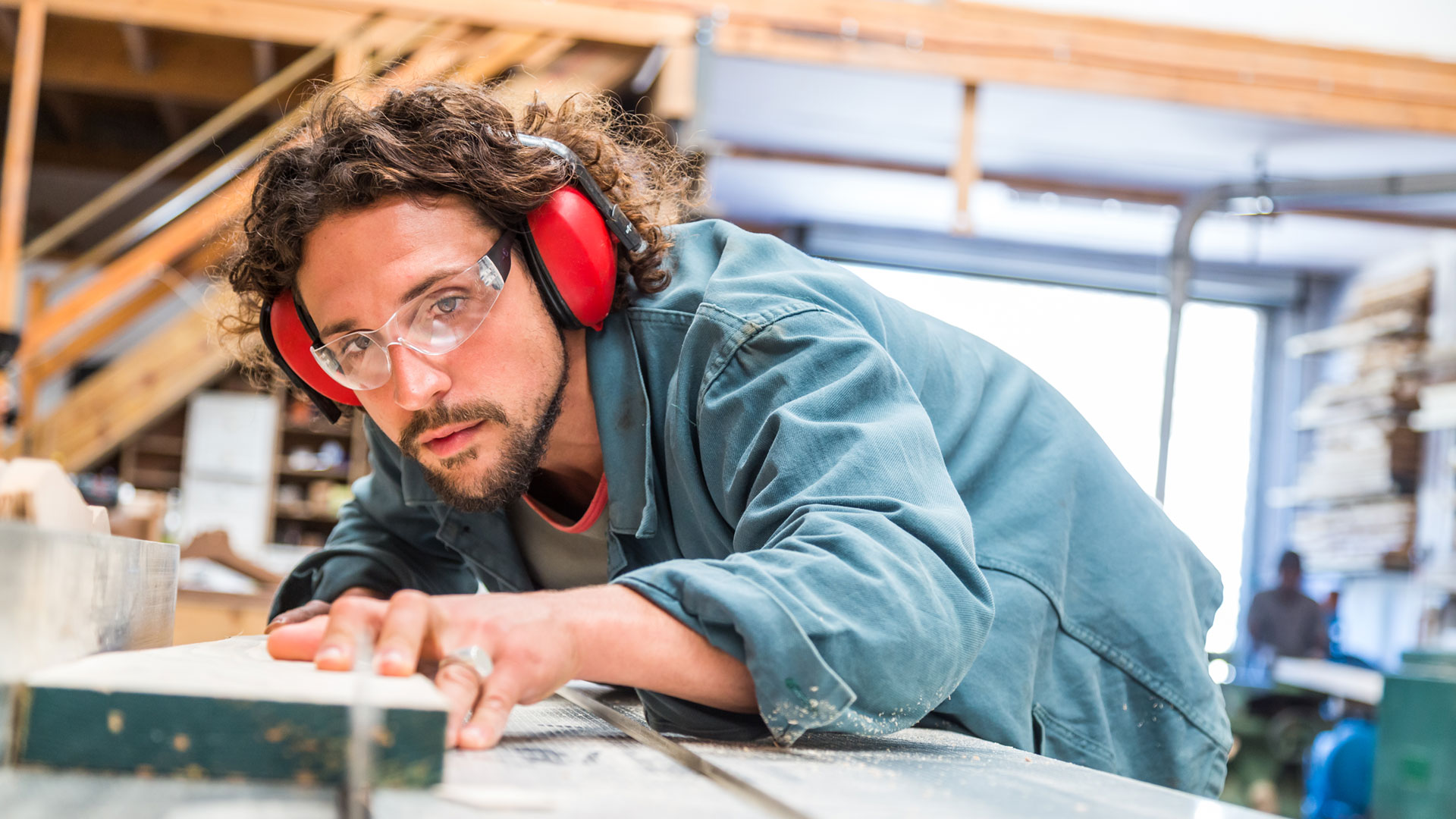 man-leaning-over-his-work-bench-cutting-piece-of-work-with-a-saw